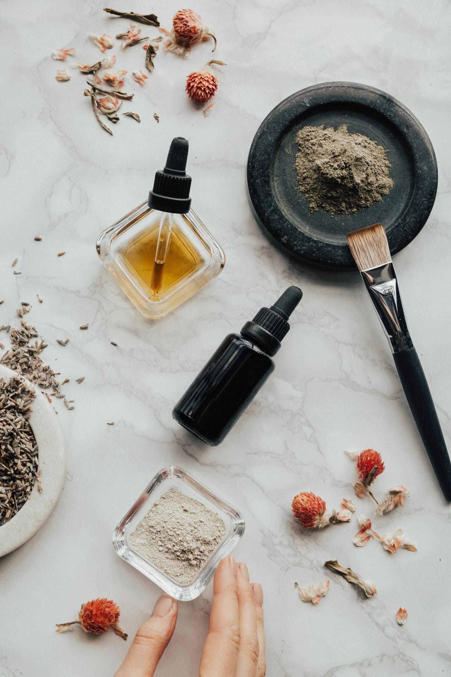 bottles of natural beard oil ingredients with dried flowers and powders on marble surface